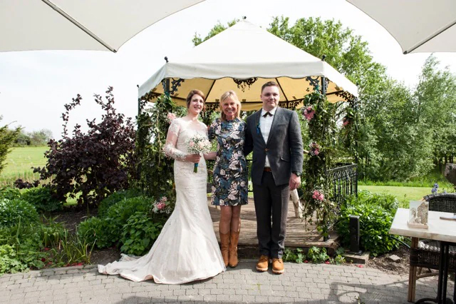 Linde stood for a photo together with the bride and groom. Behind them is a white tent and a garden.